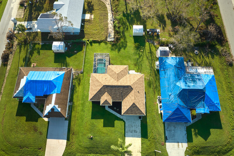 Top view of leaking house roof covered with protective tarp sheets against rain water leaks until replacement of asphalt shingles. Damage of building rooftop as aftermath of hurricane Ian in Florida